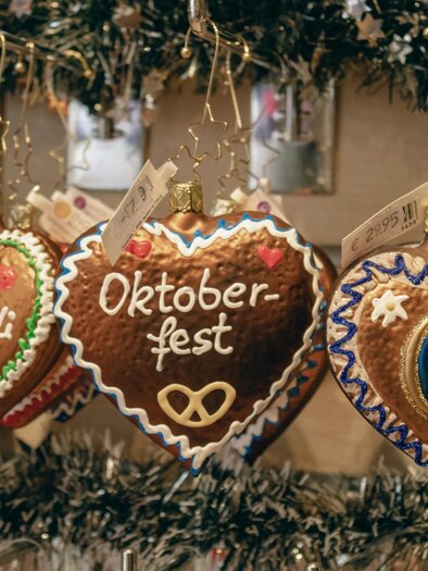 Colorful gingerbread hearts with various inscriptions, including "Oktoberfest". They are decoratively hanging at a stand. | © marlene-haiberger-unsplash