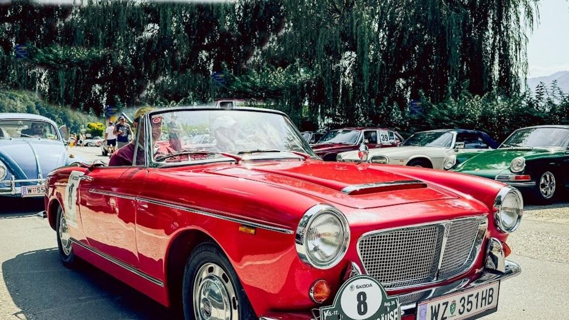 Ein rotes Cabrio steht auf einer Straße umgeben von anderen klassischen Autos. Im Hintergrund sind Berge und Bäume zu sehen. | © Ewald Schneeberger