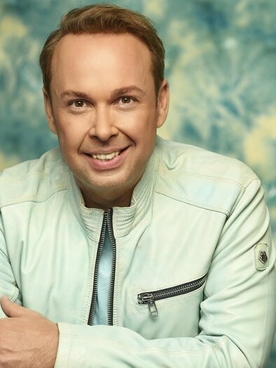 A man is smiling in a bright jacket in front of a colorful background. He is displaying a friendly and positive aura. | © Manfred_Esser