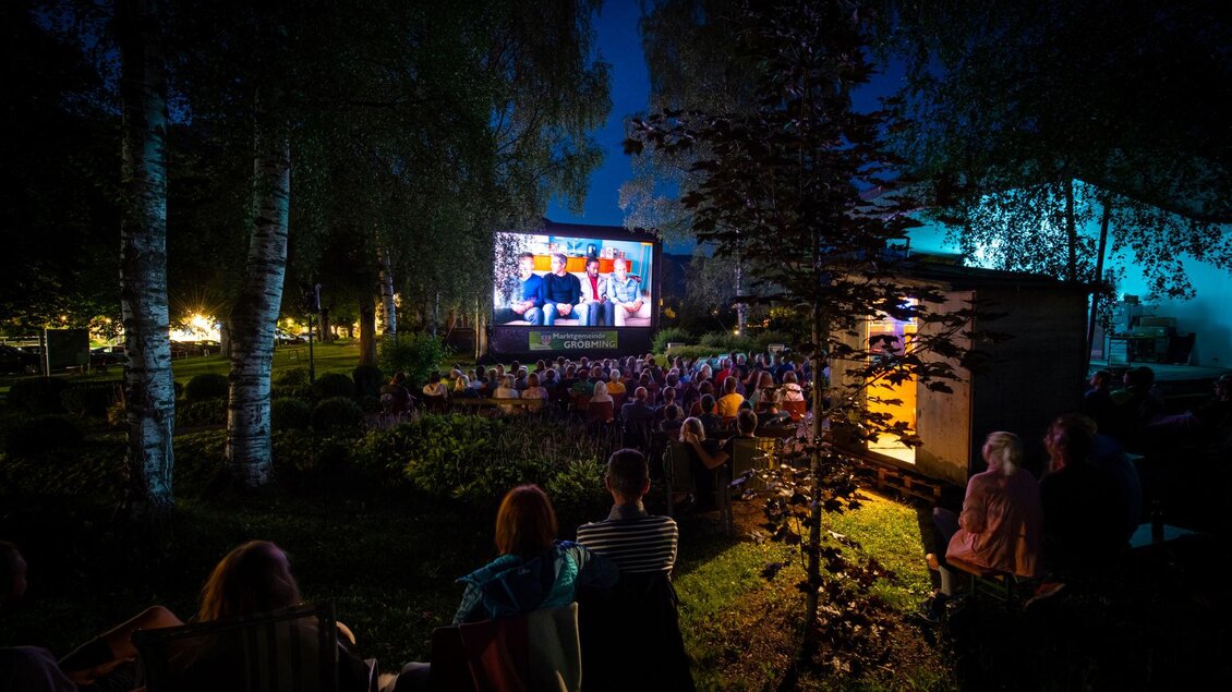 Eine Outdoor-Kinoveranstaltung bei Nacht mit vielen Zuschauern. Ein großer Bildschirm zeigt einen Film, umgeben von Bäumen und sanfter Beleuchtung. | © Christoph Huber