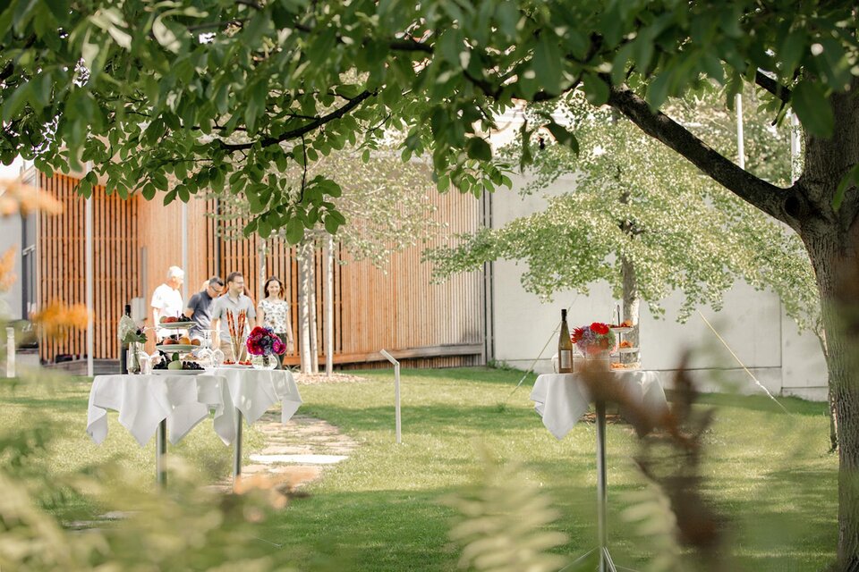 Ein schöner Garten mit gedeckten Tischen und einer entspannenden Atmosphäre. Im Hintergrund sind Personen in lebhaftem Austausch zu sehen. | © Stieglerhaus - achromaticphotography