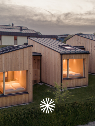 Modern, cozily illuminated wooden houses in a tranquil evening atmosphere. | © biYou - das Ecoquartier in den Bergen