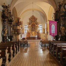Eine stille Kirche mit Holzbankreihen und einem prächtigen Altar im Hintergrund. Die Wände sind reich verziert und es gibt große Fenster, die Licht hineinlassen. | © Pollhammer