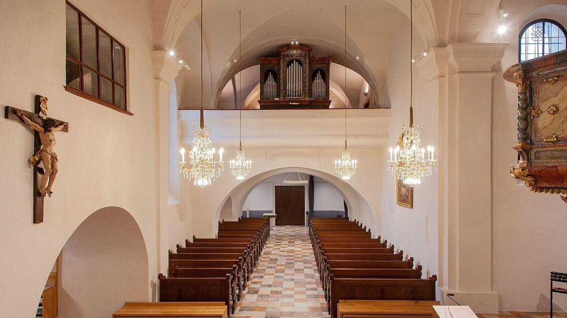 Eine helle Kirche mit einer Orgel und einem Kreuz an der Wand. Die Sitzbänke sind ordentlich in mehreren Reihen aufgestellt. | © Tourismusverband Oststeiermark/Robert Hahn
