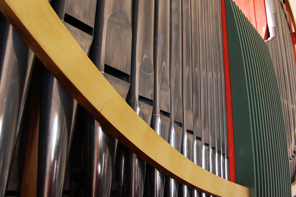Ein musikalisches Instrument mit glänzenden Metallrohren und farbigen Akzenten. Die Bildkomposition zeigt die geschwungene Form und Struktur des Instruments.