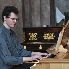 Ein Mann spielt Klavier in einem eleganten Raum. Im Hintergrund sind reich verzierte Möbel zu sehen. | © TVB Murau