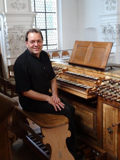 Ein Mann sitzt an einer historischen Orgel in einem hellen Kirchenraum. Die Orgel hat Holzoberflächen und ein klassisches Design. | © Heinrich Wimmer