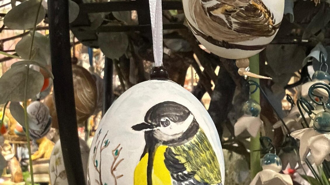 Zwei dekorierte Ostereier hängen an einer Wand. Eines zeigt einen bunten Vogel, das andere ist schlicht gehalten. | © Schloss Kornberg