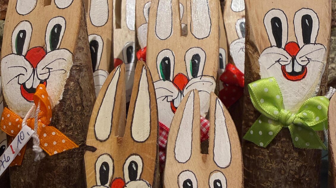 Bunte Hasenfiguren aus Holz mit fröhlichen Gesichtern und bunten Schleifen. Sie sind für Osterdekorationen gestaltet. | © Schloss Kornberg