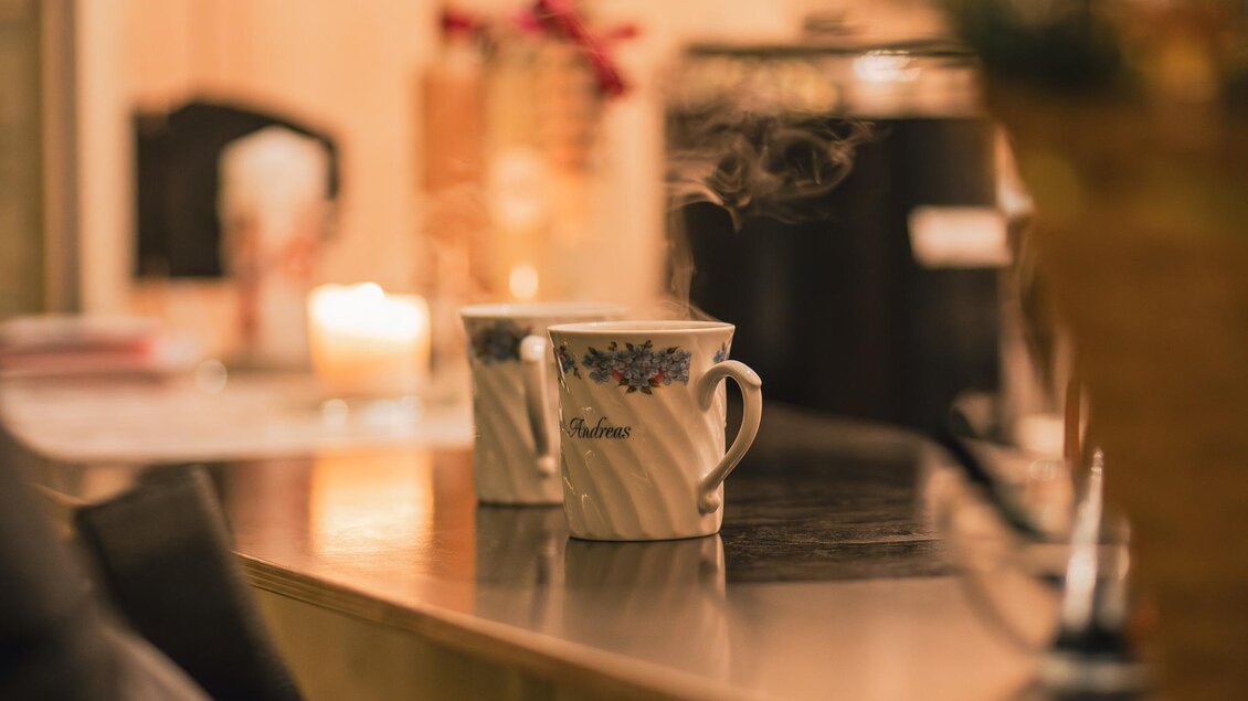 Zwei Tassen dampfenden Kaffees stehen auf einem Tisch. Im Hintergrund sind verschwommene Elemente einer gemütlichen Umgebung zu sehen. | © Ebner Maria
