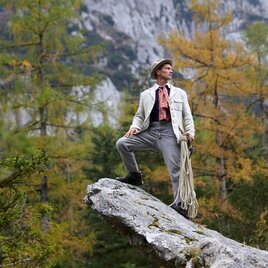 Ein Mann steht stolz auf einem Felsen in der Natur. Im Hintergrund sind Bäume und Berge zu sehen. | © Tauroa