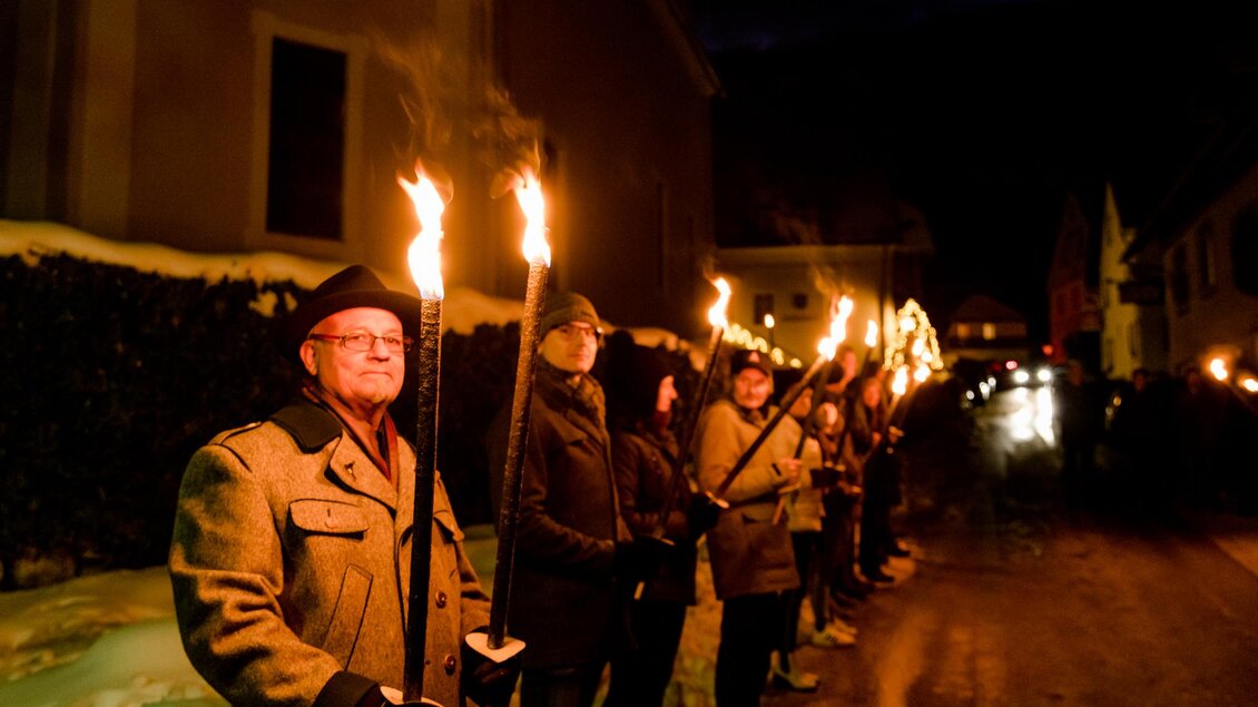 Eine Gruppe von Menschen steht in einer Straße, jeder hält eine Fackel in der Hand. Es ist Nacht und die Umgebung ist schneebedeckt. | © Region Graz-Mias Photoart