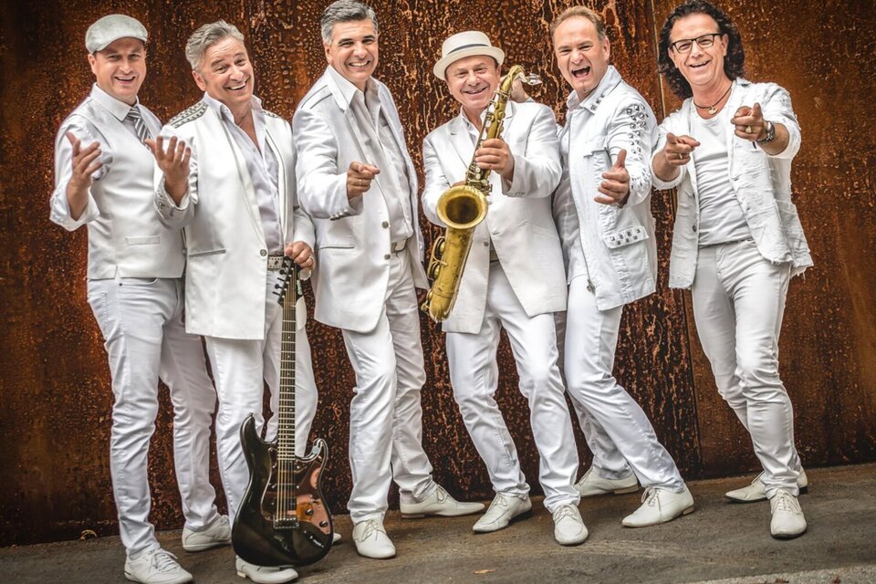 Eine Gruppe von sechs Musikern in weißen Anzügen, die fröhlich posieren. Ein Saxophonist hält sein Instrument, während die anderen Instrumente präsentieren. | © BePo