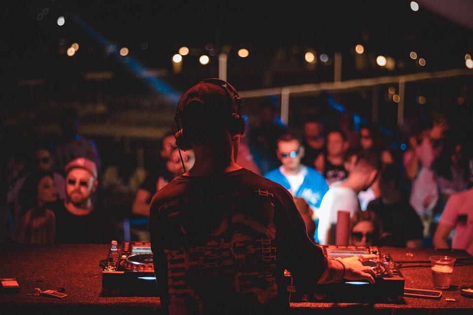 Ein DJ steht hinter einem Mischpult und spielt Musik für ein begeistertes Publikum. Die Atmosphäre ist lebhaft mit bunten Lichtern und fröhlichen Menschen. | © pixabay.com