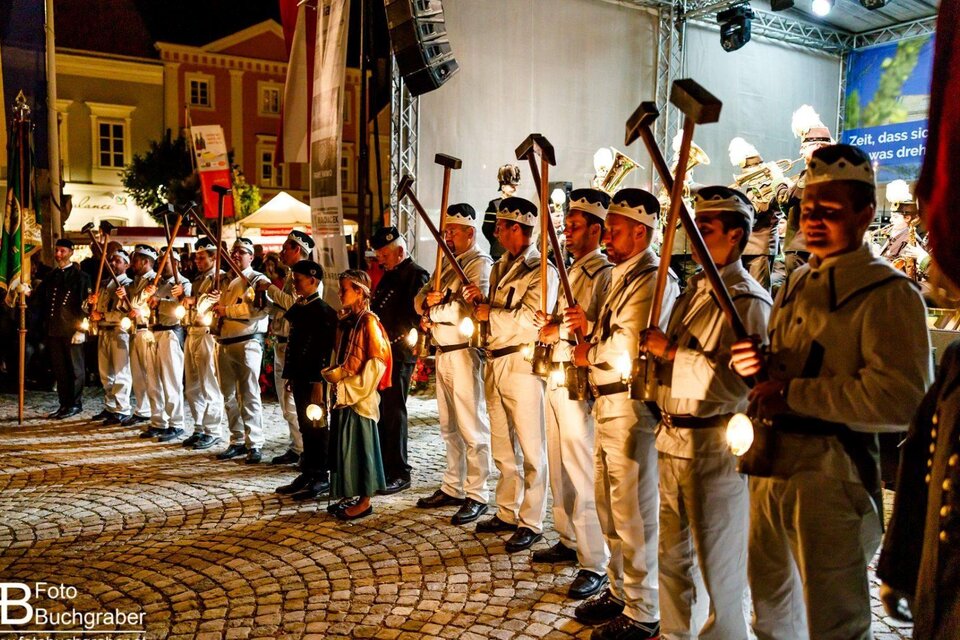 Eine Gruppe von Menschen in historischen Uniformen steht auf einem Platz. Sie halten Laternen und Werkzeuge in der Hand, während eine festliche Atmosphäre herrscht. | © Foto Buchgraber