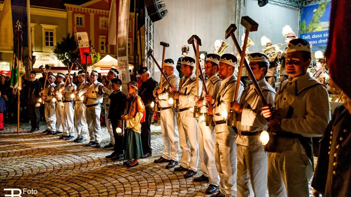 Eine Gruppe von Menschen in historischen Uniformen steht auf einem Platz. Sie halten Laternen und Werkzeuge in der Hand, während eine festliche Atmosphäre herrscht. | © Foto Buchgraber