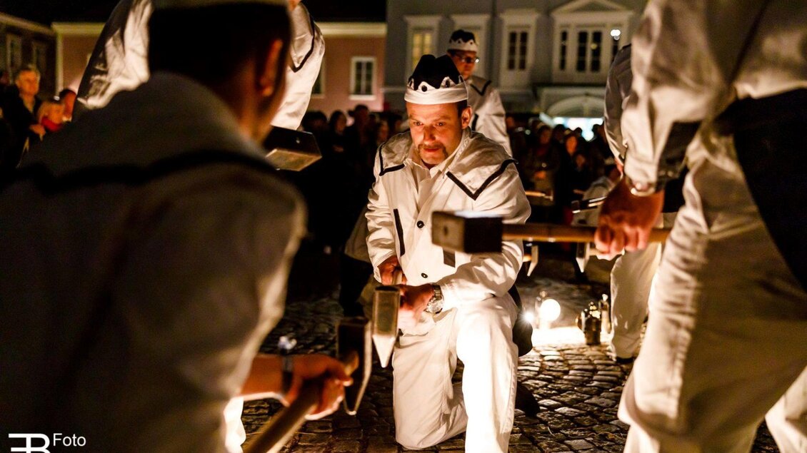 Ein nächtliches Fest mit Menschen in weißen Uniformen, die sich um eine Lichtquelle versammeln. Die Atmosphäre ist festlich und lebhaft, mit einer großen Menschenmenge im Hintergrund. | © Foto Buchgraber