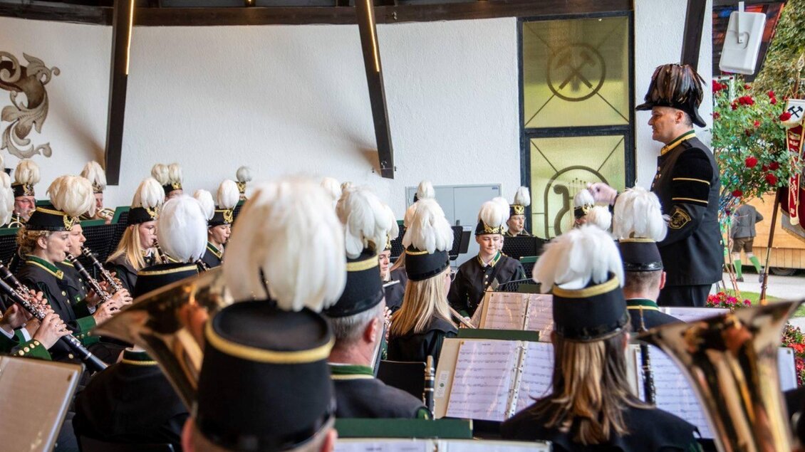 Ein Blasorchester spielt in einem festlich dekorierten Raum. Der Dirigent leitet die Musiker, die in traditionellen Uniformen mit Federhauben gekleidet sind. | © Erich Kainzinger