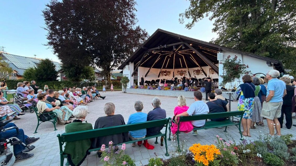 Ein Konzert im Freien mit vielen Zuschauern auf Bänken. Die Bühne ist von Pflanzen umgeben und die Atmosphäre ist festlich. | © Salinenmusik Altaussee_Theresa Rastl_Robert Leu