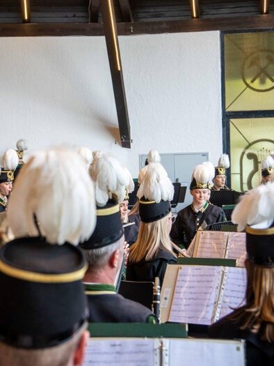 A brass band is playing in a festively decorated room. The musicians are wearing uniforms with striking hats and are focusing on the conductor. | © Erich Kainzinger