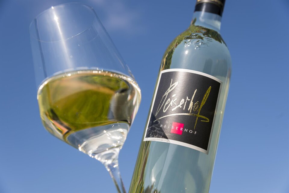 Eine Flasche Weißwein steht neben einem Weinglas. Im Hintergrund ist ein klarer blauer Himmel zu sehen. | © Peiserhof