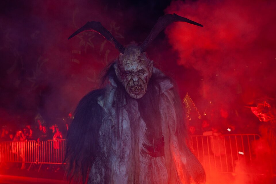 Eine furchteinflößende Perchtenfigur mit Hörnern beim Perchtenlauf in Gratkorn in rotem Nebel | © Graz Tourismus-Harry Schiffer