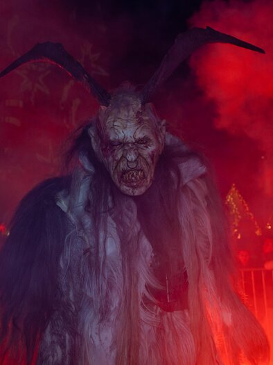 Eine furchteinflößende Perchtenfigur mit Hörnern beim Perchtenlauf in Gratkorn in rotem Nebel | © Graz Tourismus-Harry Schiffer