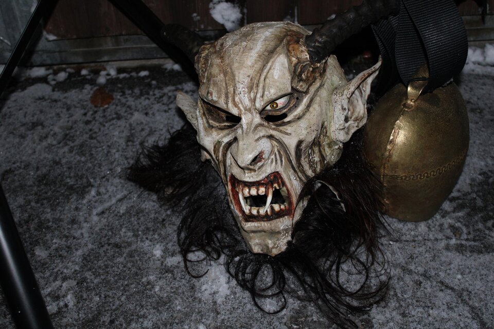 Eine gruselige Maske mit Hörnern und fletschenden Zähnen liegt auf dem Boden. Neben der Maske befindet sich eine große Glocke. | © Tourismusverband Oststeiermark