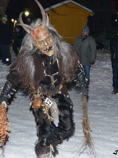 A creepily disguised demon with horns and a wild costume stands in the snow. Around him, people in warm clothing can be seen. | © Joglland Teifl