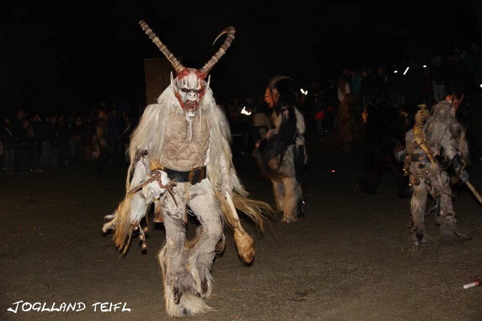 Eine festliche Umzug mit traditionellen Kostümen und Masken. Die Teilnehmer bewegen sich in einer nächtlichen Umgebung. | © Jogllandteifl