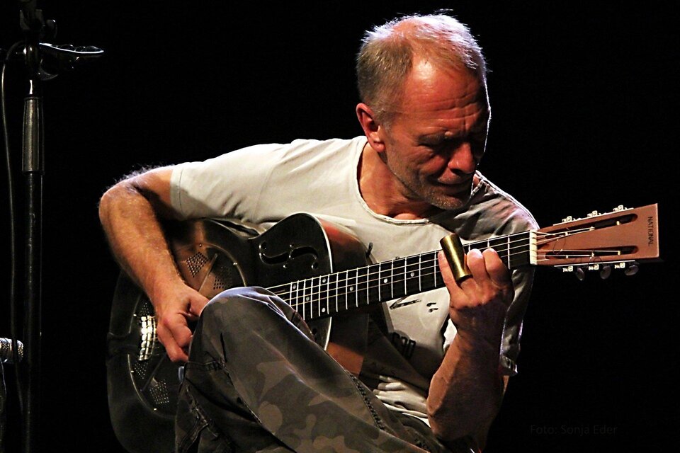 Ein Musiker spielt Gitarre auf der Bühne. Er trägt ein einfaches T-Shirt und konzentriert sich auf seine Musik. | © Sonja Eder