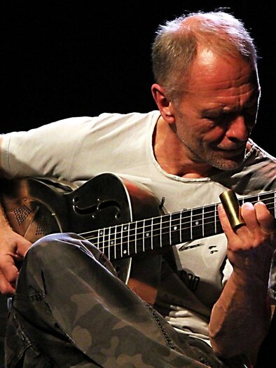 Ein Musiker spielt Gitarre auf der Bühne. Er trägt ein einfaches T-Shirt und konzentriert sich auf seine Musik. | © Sonja Eder