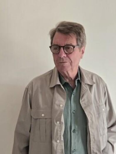 Ein älterer Mann steht vor einer neutralen Wand. Er trägt eine bequeme Jacke und eine Brille. | © Christiana Pock-Rosei