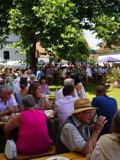 Ein belebter Garten mit zahlreichen Gästen, die an Tischen sitzen und essen. Im Hintergrund sind Bäume und Festzelte zu sehen. | © Peter Schandor