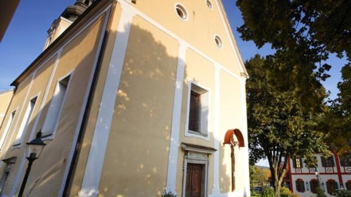 Eine gelbe Kirche mit einer schönen Fassade und großen Fenstern. Der umliegende Garten ist gepflegt und von Bäumen umgeben. | © Pfarre BW