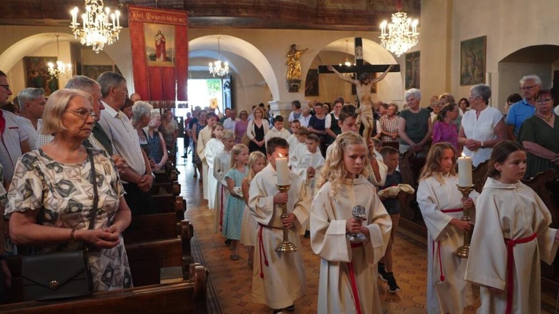 Eine Kirche, in der viele Menschen versammelt sind. Kinder in weißen Gewändern tragen Kerzen und gehen den Mittelgang entlang. | © Peter Schandor