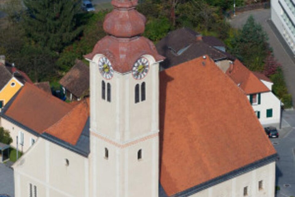 Eine Kirche mit einem markanten Kirchturm und einem roten Dach. Umgeben von Wohnhäusern und Bäumen. | © Marktgemeinde Eibiswald