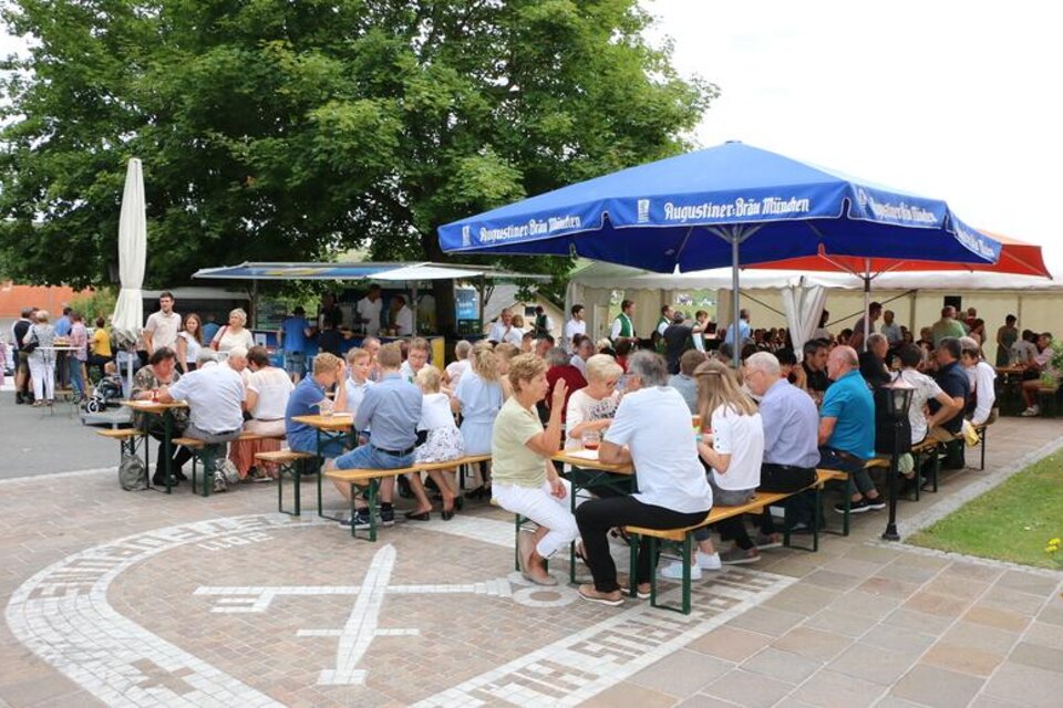 Eine belebte Außenveranstaltung mit vielen Menschen, die an Tischen sitzen und essen. Im Hintergrund sind Markisen und Bäume zu sehen. | © Pfarre Hatzendorf