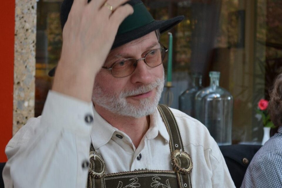 Ein Mann mit Brille und einem traditionellen Hut sitzt in einem gemütlichen Restaurant. Er trägt eine Lederhose und hat ein freundliches Gesicht. | © Familie Michelitsch