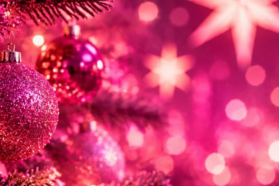 Ein festlich geschmückter Weihnachtsbaum mit glitzernden, rosa Kugeln. Im Hintergrund leuchten bunte Lichter und Sterne. | © mit KI generiert