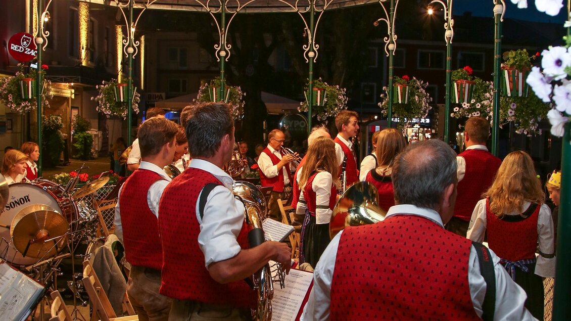 Eine Gruppe von Musikern in traditionellen Trachten spielt in einem Pavillon. Die Atmosphäre ist festlich und von bunten Blumen umgeben. | © Harald Steiner