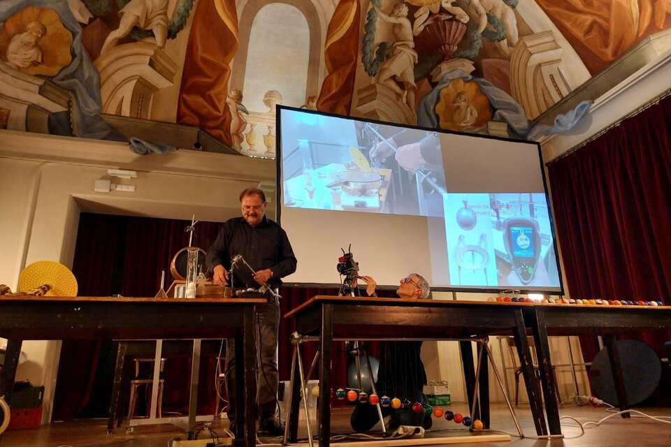 Eine Präsentation in einem historischen Raum mit aufwändiger Deckenmalerei. Zwei Personen stehen an Tischen mit wissenschaftlichen Geräten und einem Bildschirm im Hintergrund. | © Echophysics
