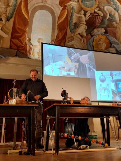 Eine Präsentation in einem historischen Raum mit aufwändiger Deckenmalerei. Zwei Personen stehen an Tischen mit wissenschaftlichen Geräten und einem Bildschirm im Hintergrund. | © Echophysics