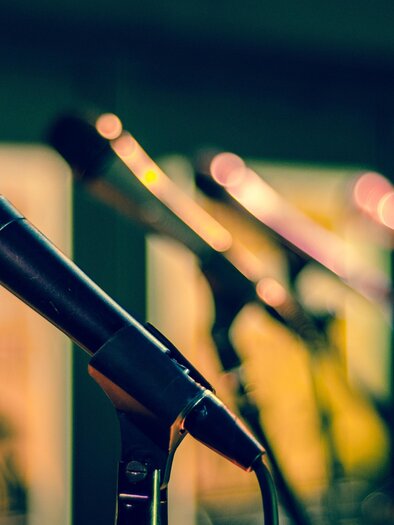 A microphone is in the foreground, while several other microphones are blurred in the background. The scene conveys a musical atmosphere. | © Pixabay