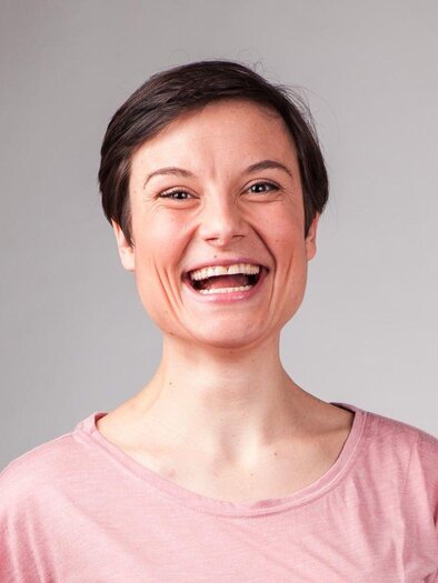 Eine lächelnde Frau mit kurzen Haaren trägt ein rosa T-Shirt. Der Hintergrund ist neutral und hell. | © Reinhard-Fröhlich-Steiner