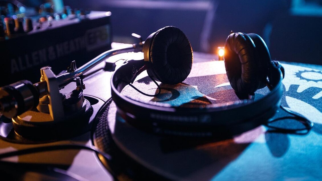 Ein DJ-Setup mit Kopfhörern und einem Plattenspieler. Die Szene ist schwach beleuchtet und vermittelt eine clubartige Atmosphäre. | © pixabay.com