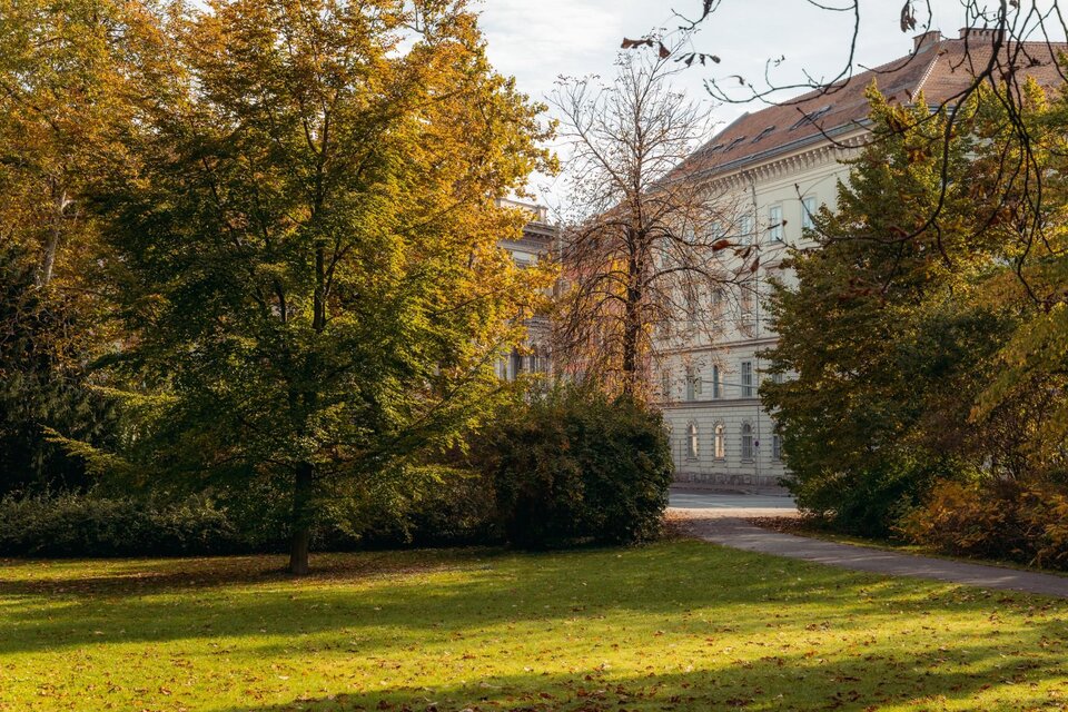 Herbstlich gefärbte Bäume und Grünflächen im Stadtpark Graz mit historischem Gebäude im Hintergrund. | © Region Graz-studio draussen