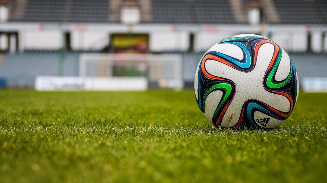 Ein Fußball liegt auf dem grünen Rasen eines Stadions. Im Hintergrund sind leere Sitzplätze zu sehen. | © pixabay.com