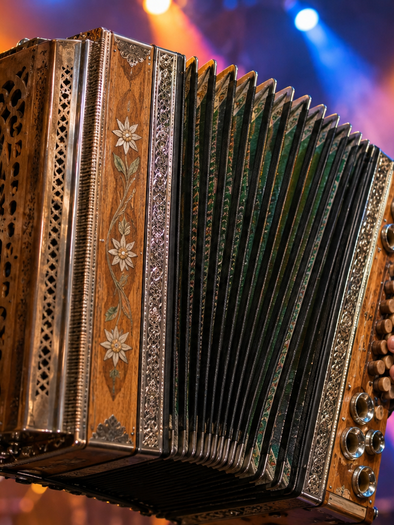 Ein Musiker spielt eine verzierte Steirische Harmonika auf einer Bühne mit farbigen Scheinwerfern. | © ChatGPT-Christine Rotschädl