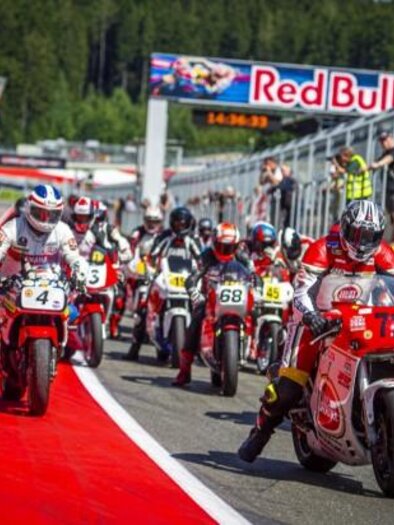 A group of motorcycles starts on a racetrack. Spectators stand by the side and watch the event. | © Lucas Pripfl
